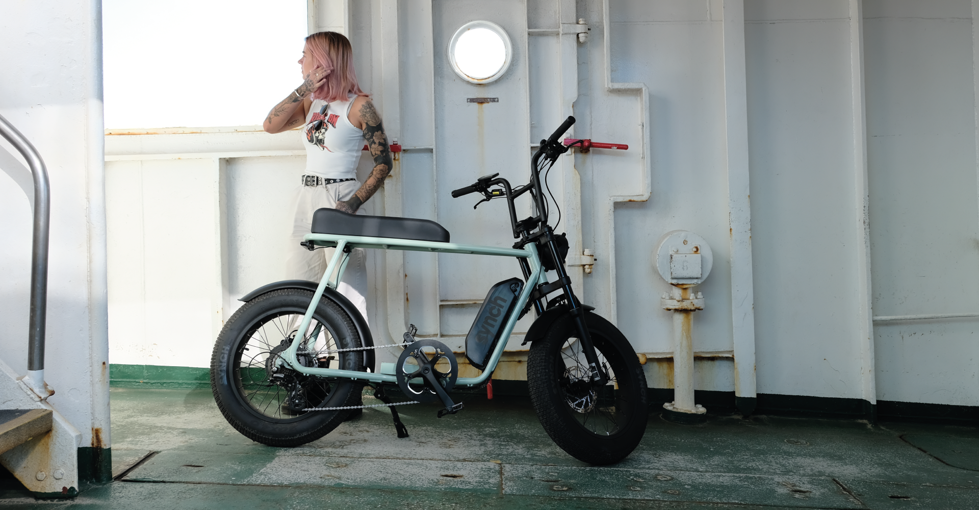 Minty colour Synch electric bikes. Bike on stand with lady stood behind.