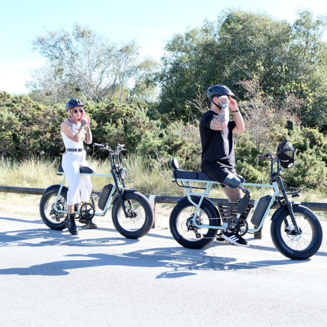 A Synch Super monkey being ridden by a lady and Longtail Monkey (two seater electric bike) being ridden by a man. Motorbike Style Ebike
