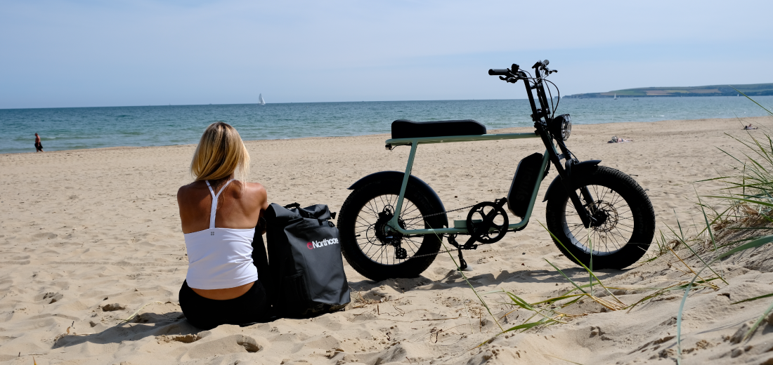 Synch fat tyre electric bike. Side on view on a beach with yoga instructor sat next to it on the sand